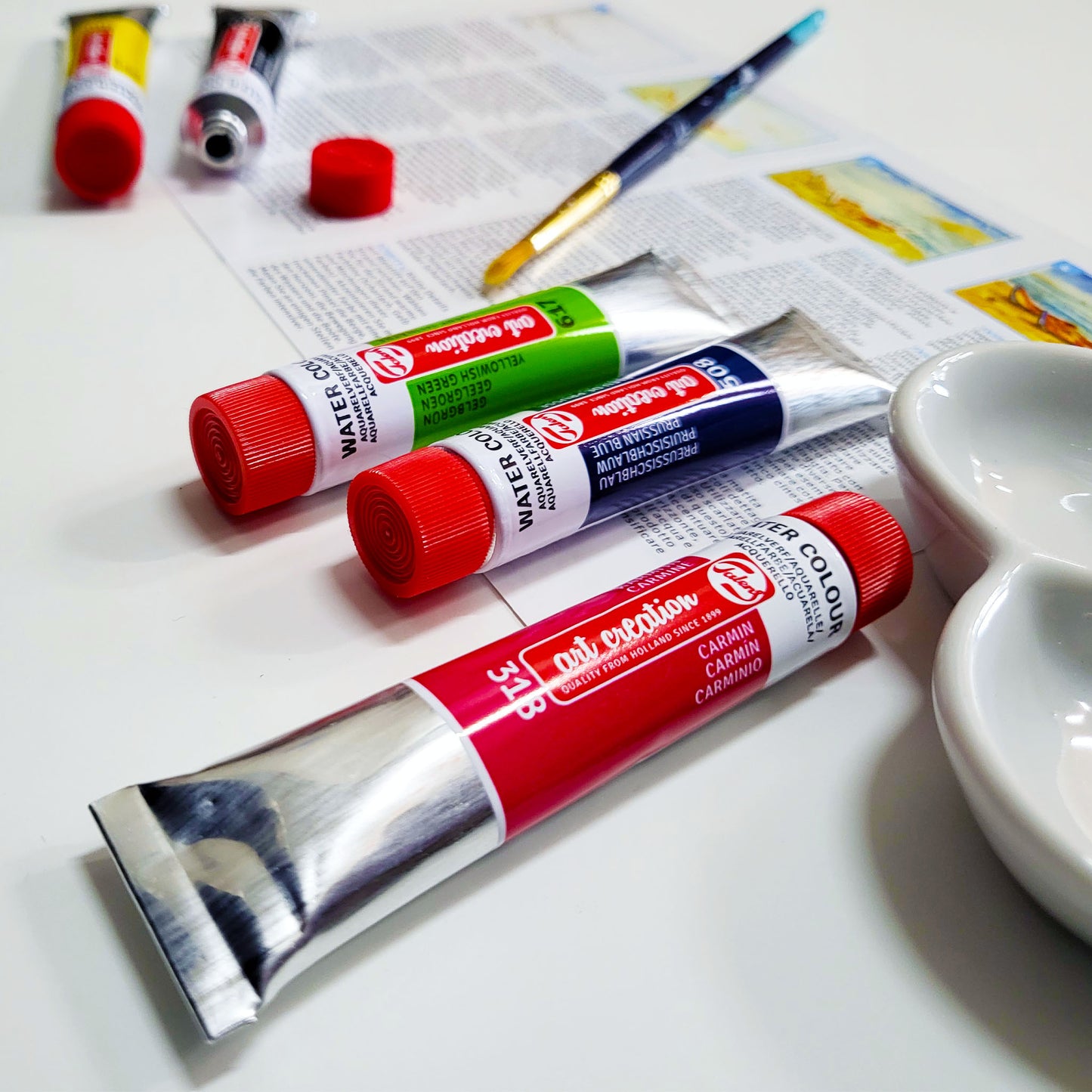 tubes of water color paint and a brush laying on top of an art article on a white table