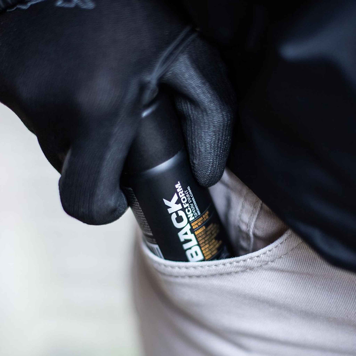 Gloved hand reaching for Montana Black 50ml pocket spray paint can