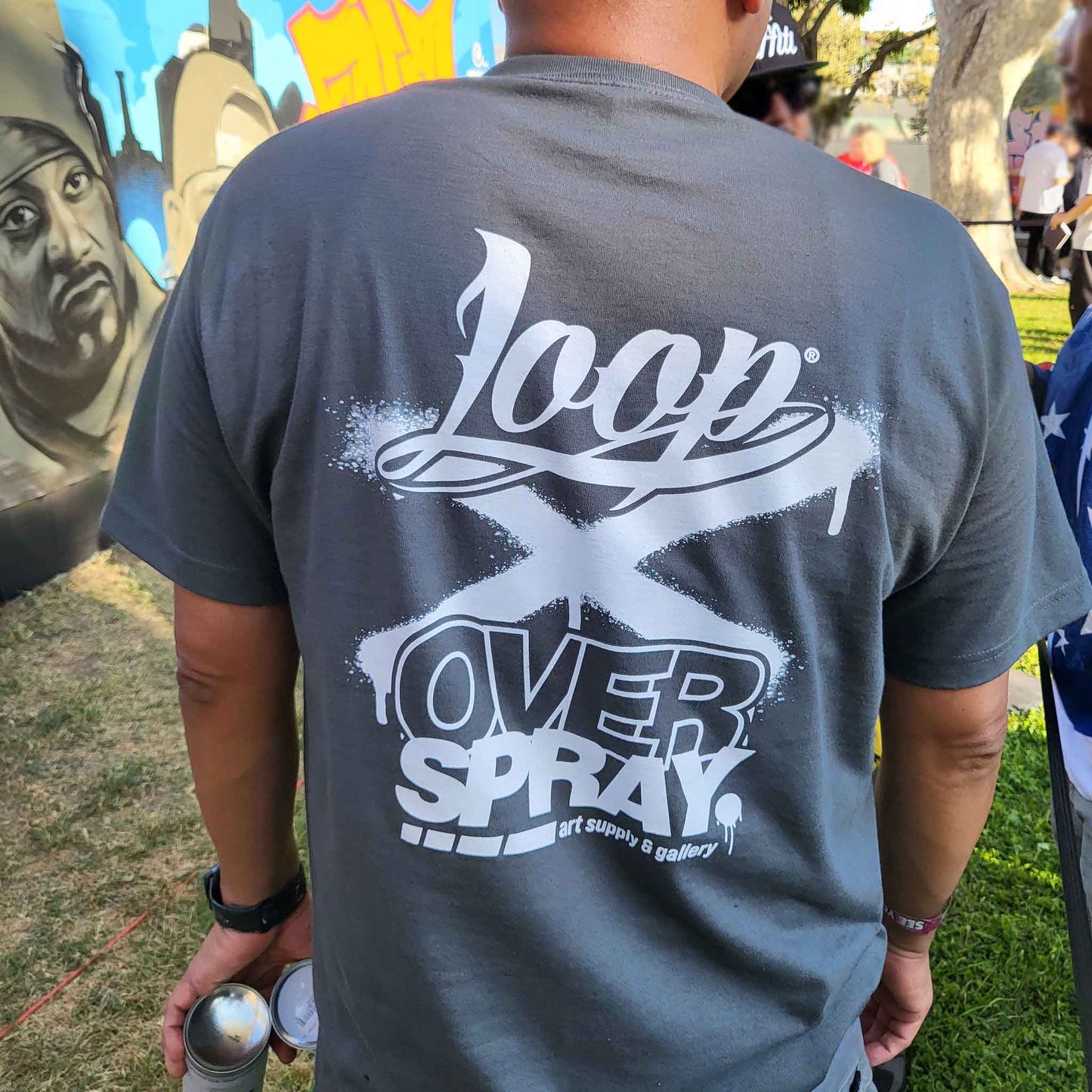 Person wearing a gray t-shirt with 'Loop X Over Spray' design, standing outdoors.