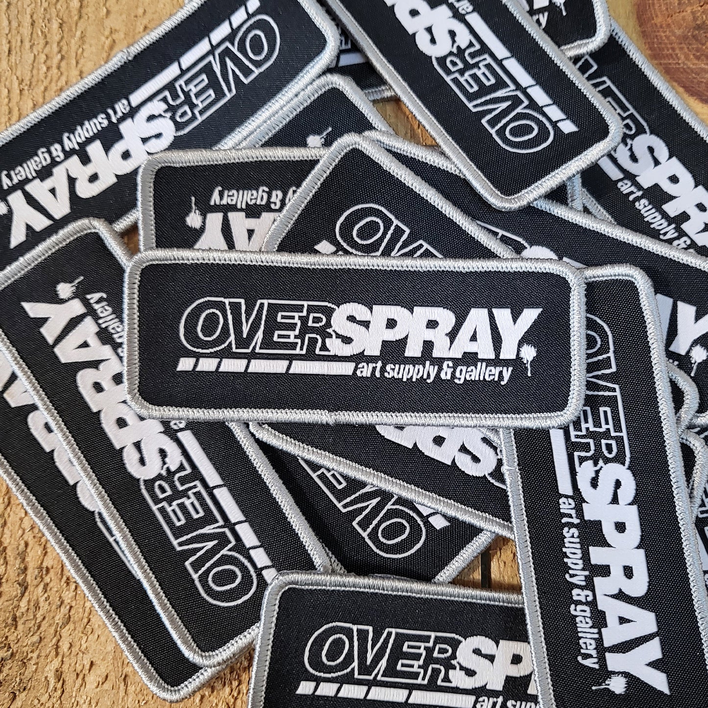 overspray logo patch in black and white with a silver frame