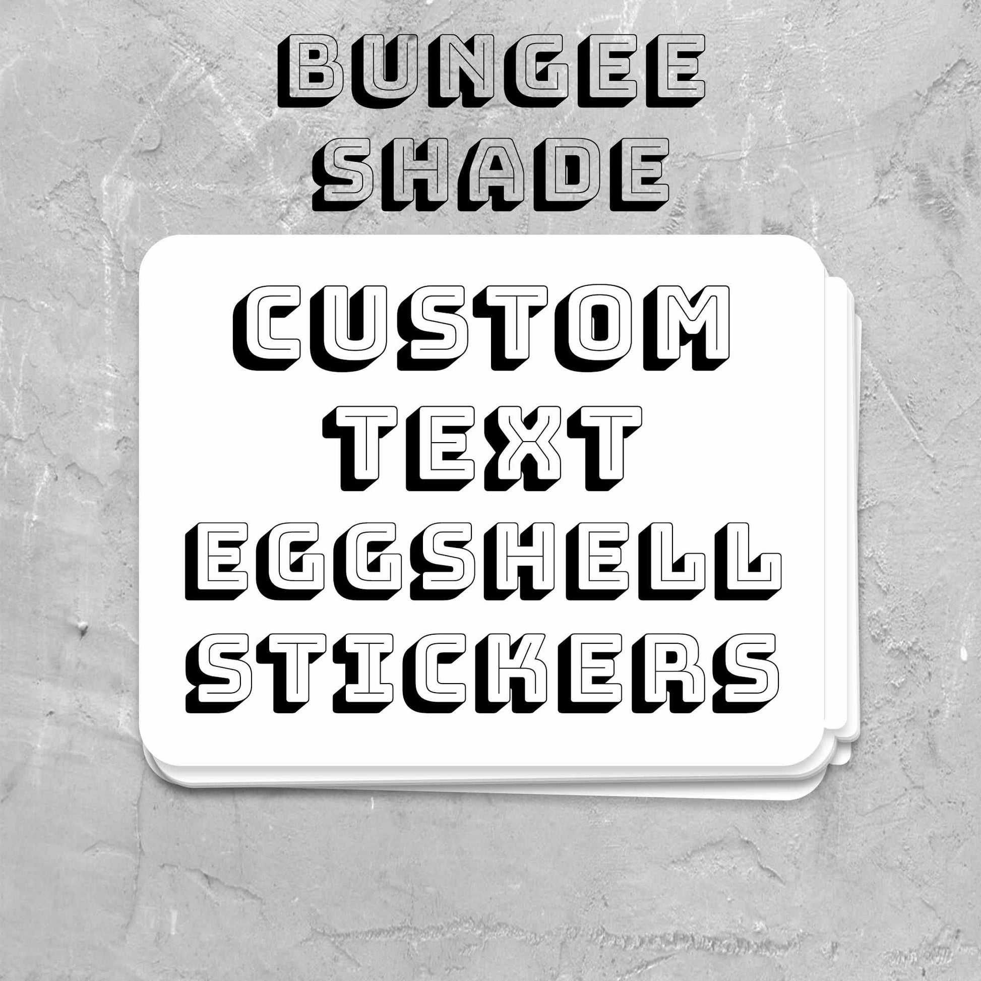 A stack of white custom text eggshell stickers with black 3D lettering, with the text 'BUNGEE SHADE' and 'CUSTOM TEXT EGGSHELL STICKERS' above it.