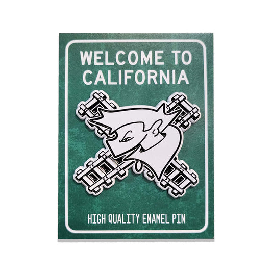 A California-themed card green backing card with an enamel pin of a black and white graffiti character with railroad tracks.