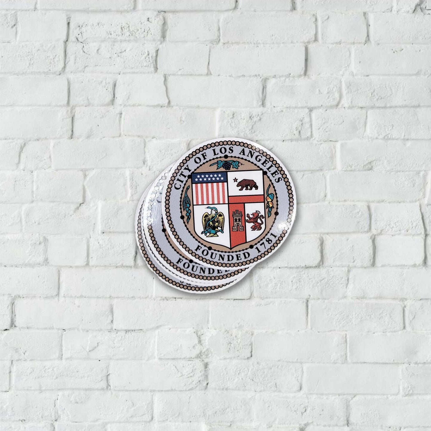 Los Angeles city seal stickers on a white brick wall.