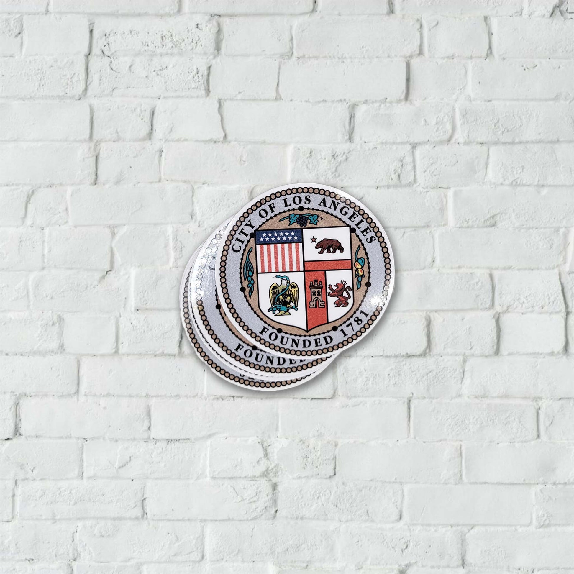 Los Angeles city seal stickers on a white brick wall.