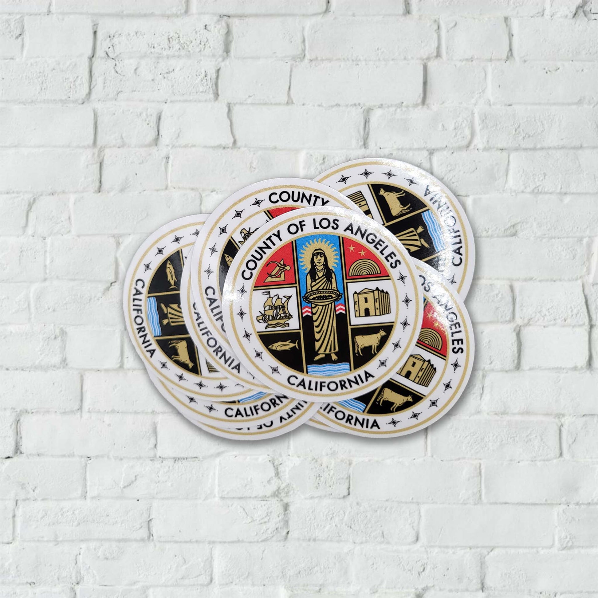 Circular stickers with the County of Los Angeles logo on a white brick wall background.