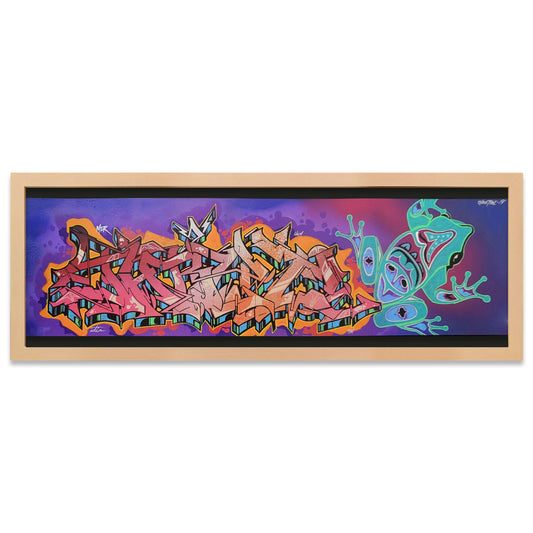A framed horizontal art print featuring colorful graffiti-style lettering on the left and a bright green frog illustration on the right, set against a purple and pink background, enclosed in a light wood frame.