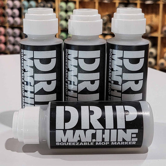 Three Drip Machine empty squeezable mop marker containers on a white surface with a blurred background.