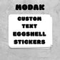 A stack of white eggshell stickers with bold black text reading 'MODAK CUSTOM TEXT EGSHELL STICKERS'.