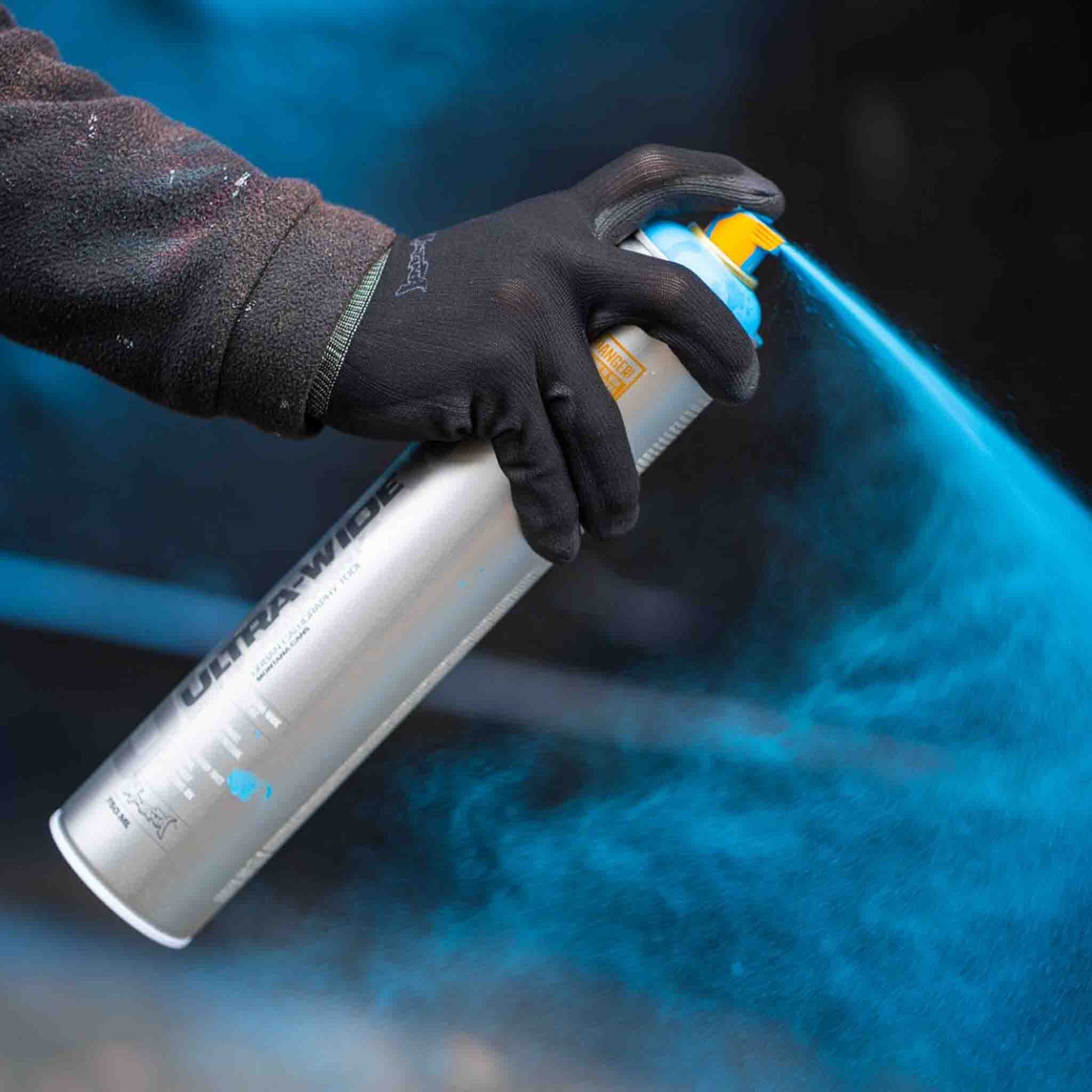 Person holding a can of Ultra Wide spray paint with blue paint spraying
