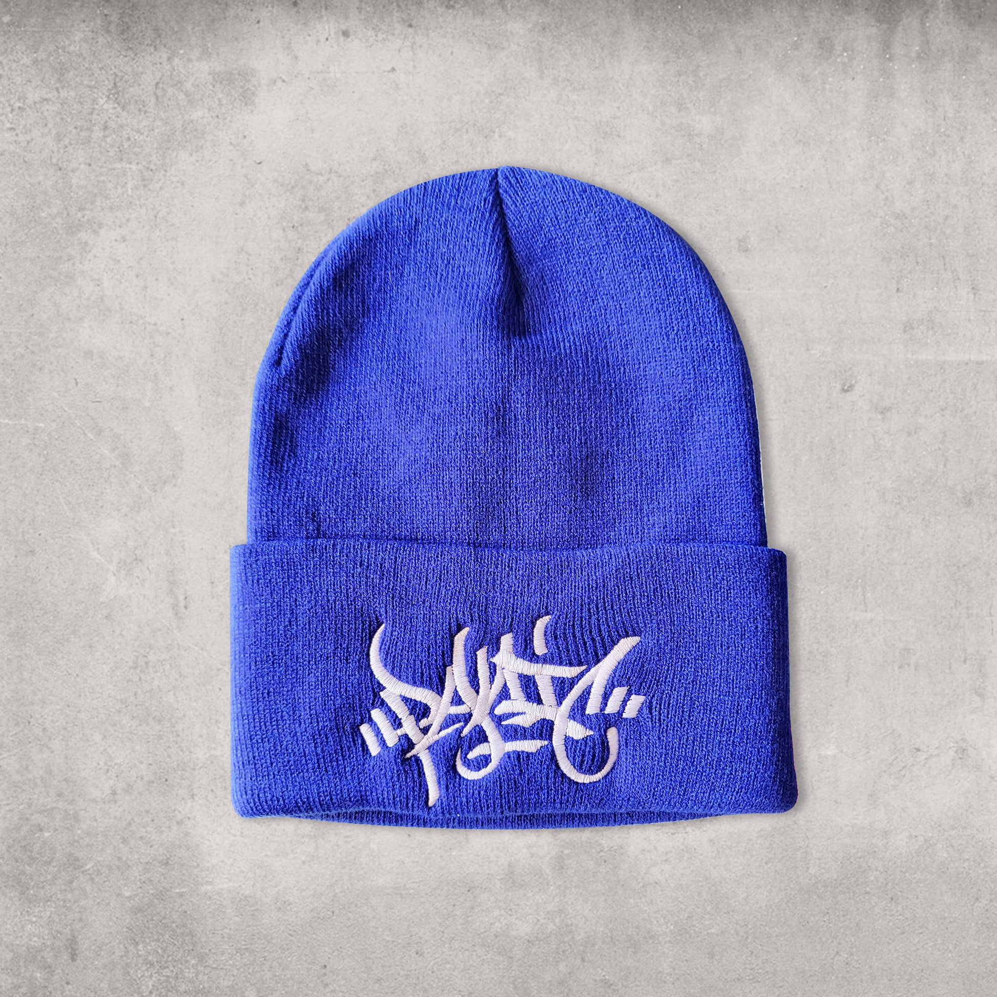 Blue beanie hat with white centered embroidery reading Panic in tag font.