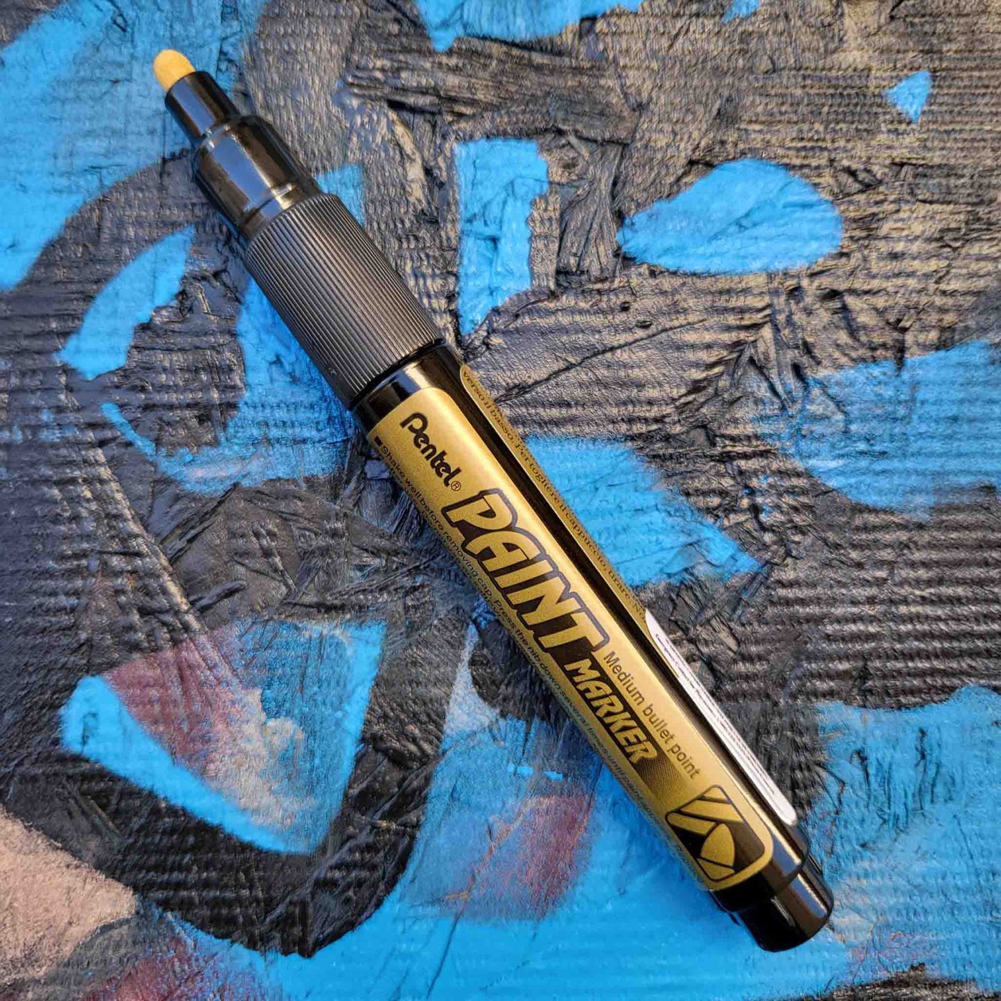 Pentel bullet point paint marker in gold on a colored background