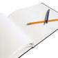 An open blank sketchbook with white pages, shown on a white background with two pens resting on top.