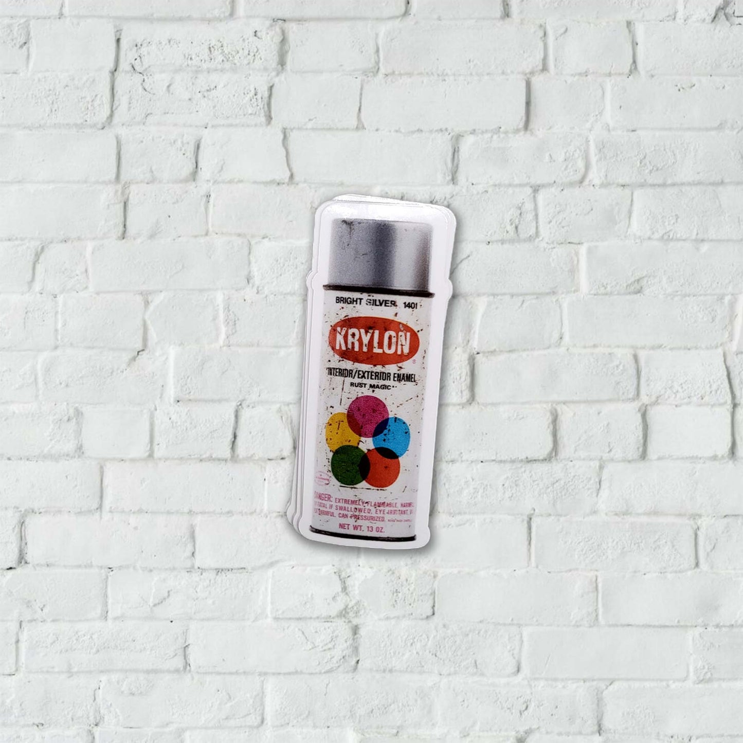 Silver Krylon spray paint can stickers on a white brick wall background.
