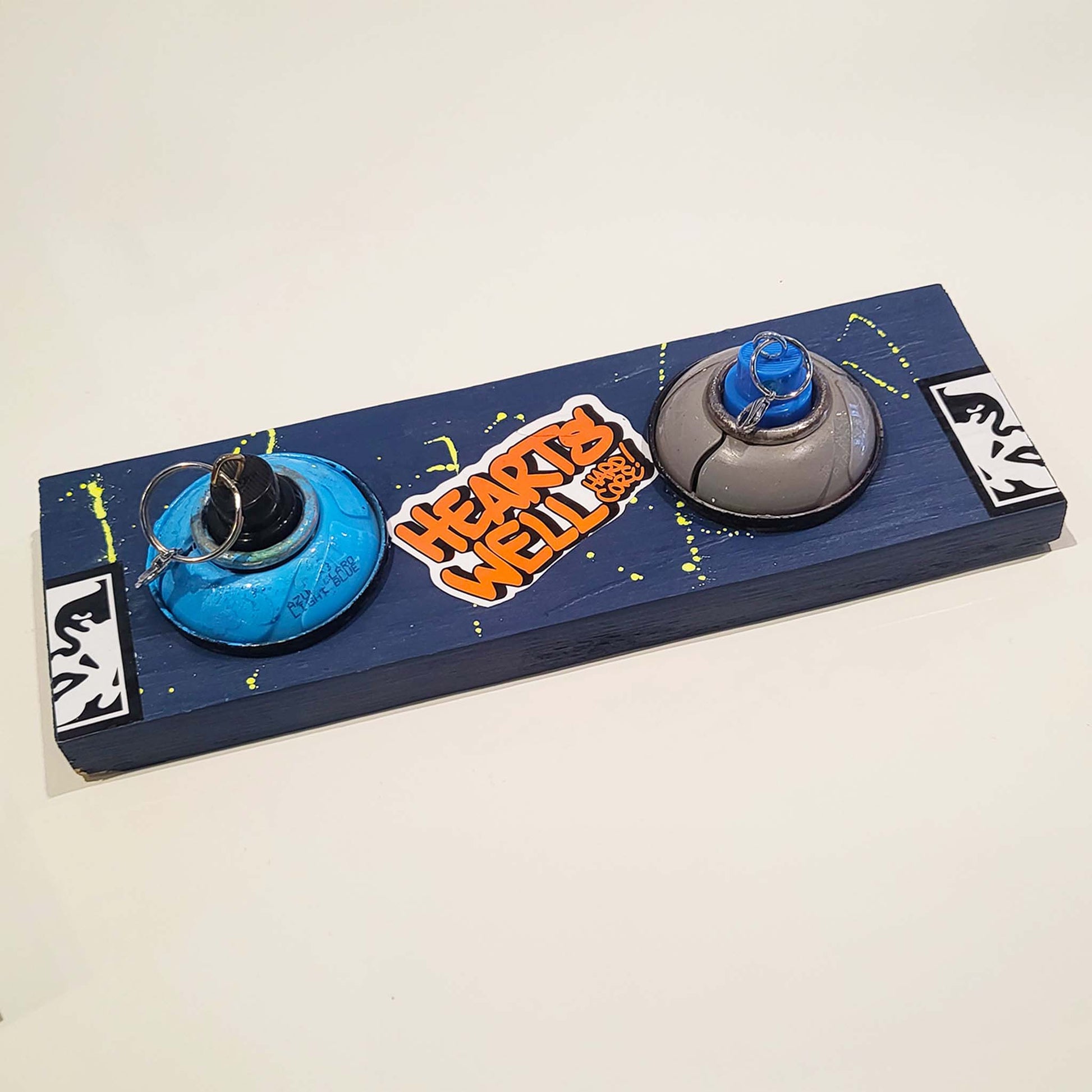 Blue keychain holder mount with paint splatters and spray paint nozzles.