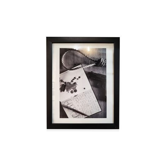Black framed black and white photo of a notebook with writing and a pen.