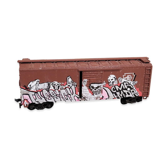 A brown miniature train boxcar with graffiti style painting ont he side.