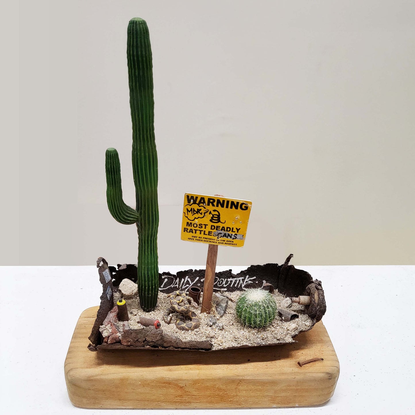 A wood block with a rusted spray paint can holding a desert diorama miniature.