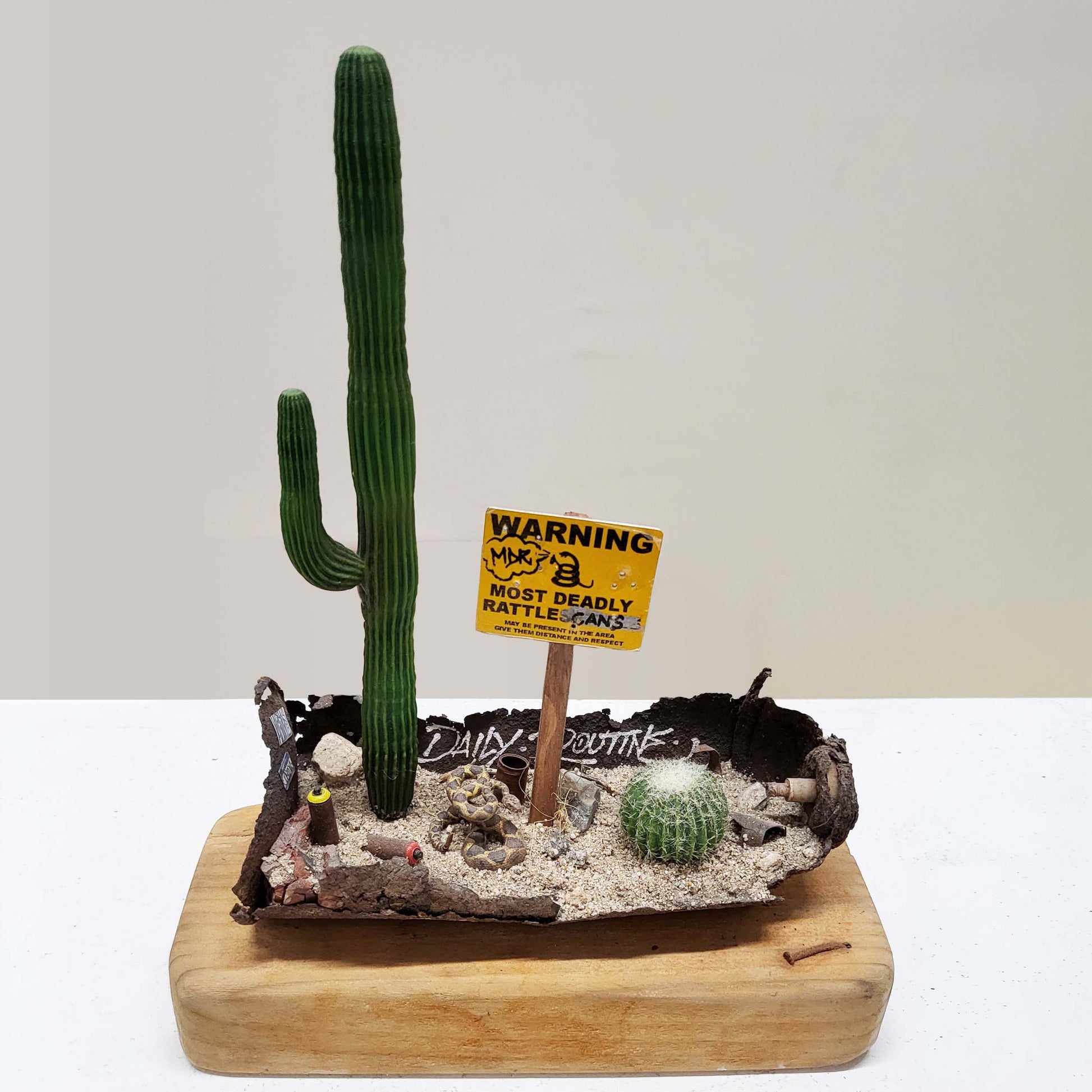 A wood block with a rusted spray paint can holding a desert diorama miniature.