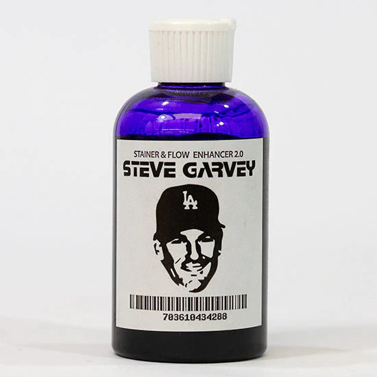 A clear bottle of purple ink with a large white cap, there's a white label on the front that reads "Strainer & flow Enhancer 2.0 - STEVE GARVEY" at the top and a high contrast image of LA Dodger's Steve Gravey's face underneath.